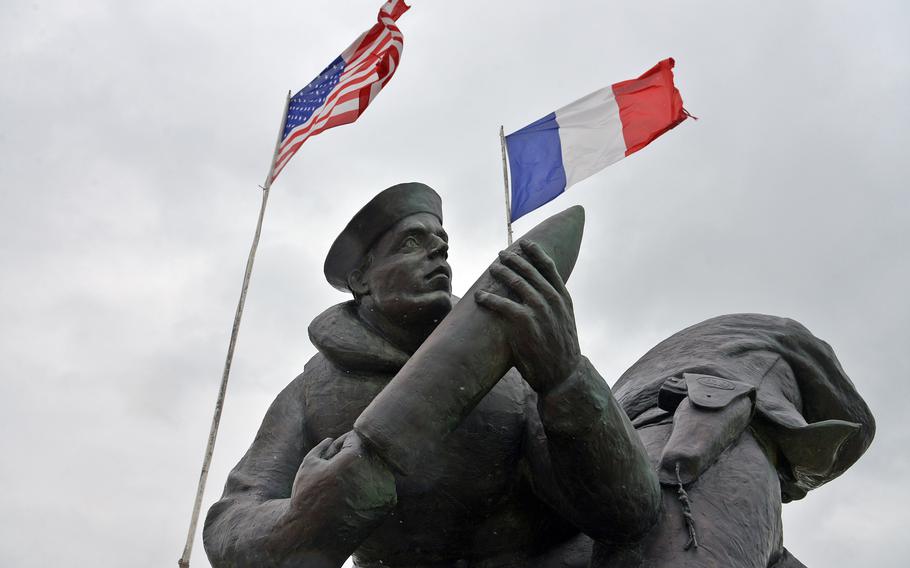 A sailor holds a shell as the American and French flags wave in the wind above the U.S. Navy monument on Utah Beach. The monument was unveiled in 2008.