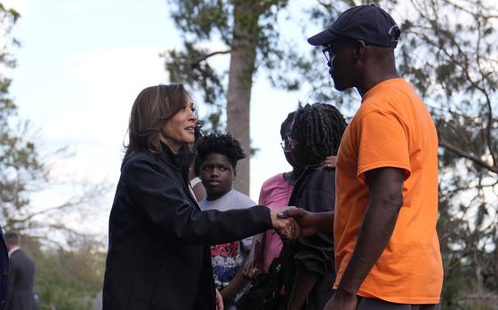 Kamala Harris shakes hands with a man in an orange shirt and blue hat.