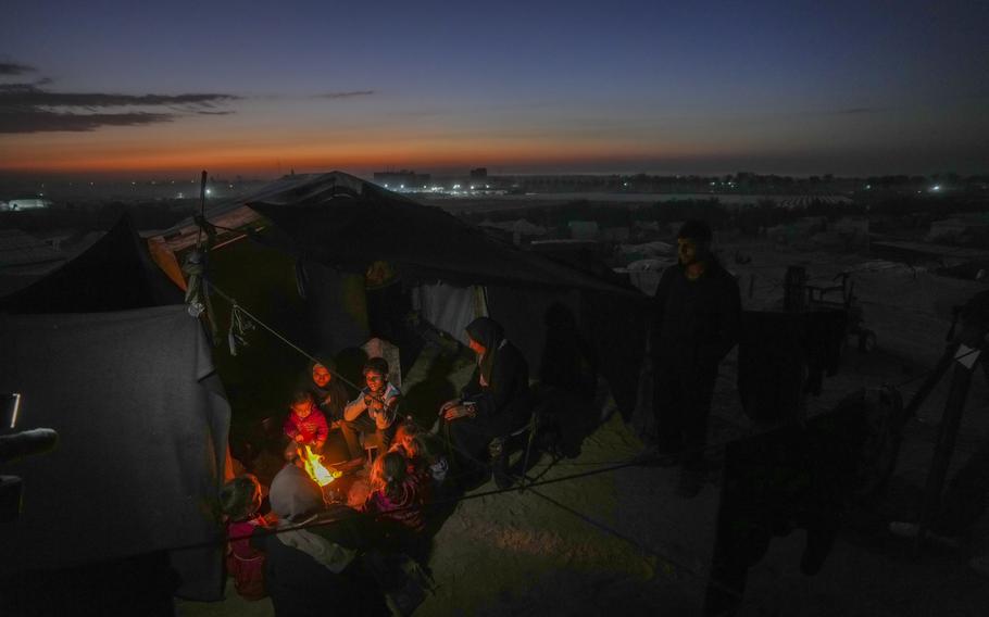 Displaced Palestinian seek warmth by a fire in a Gaza camp.