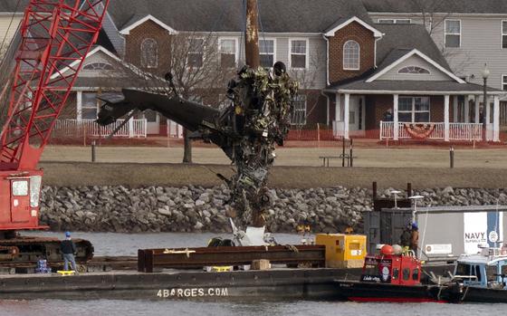 A salvage crew pulls up part of helicopter, covered in muck, from a river.