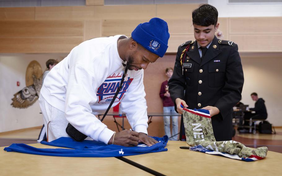 Victor Cruz, a former wide receiver for the New York Giants, signs memorabilia for a student at Vilseck High School in Germany on Nov. 7, 2024. Cruz and fellow former Giants player Brandon London visited Vilseck schools to talk to students and play a bit of tag football.