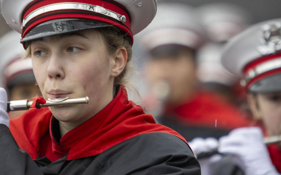 A woman in a marching band uniform plays a woodwind instrument.