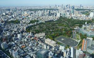 An overhead view of a helipad and green space surrounded by the skyscrapers of downtown Tokyo.