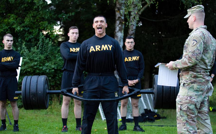 A U.S. soldier wearing a black-and-gold physical training uniform does a maximum weight deadlift.