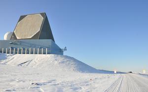 A building with a large radar on top with a snow covered roads leading past it.