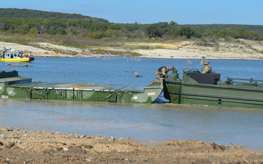 A soldier connects a bridge building boat to a piece of bridge to begin building a seven-float bridge to transport combat vehicles across Belton Lake at Fort Cavazos, Texas, as part of a division-level training exercise Nov. 3, 2023.