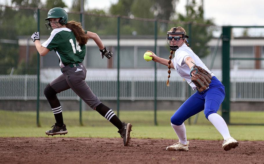 Two girls at a baseball field, one in a green uniform and the other in white.