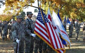 Guard members stand at attention, holding the U.S. flag and National Guard flags.