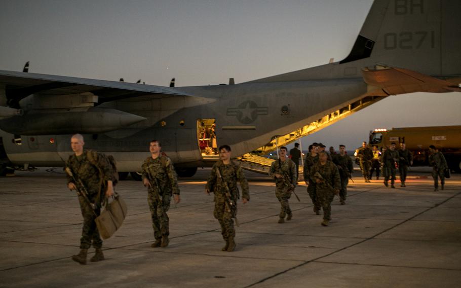 Marines walking across tarmac after getting off a military aircraft.