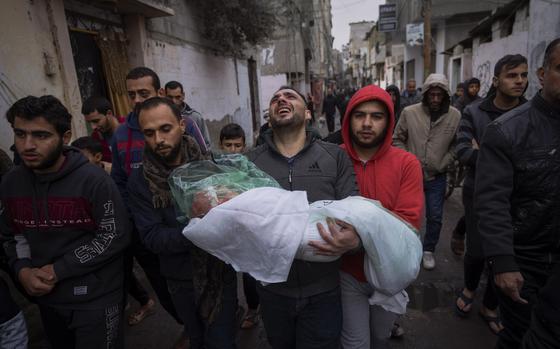 A group of Palestinian men walk down a street, with one, his face twisted in anguish, carrying the plastic and blanket wrapped body of a young girl.