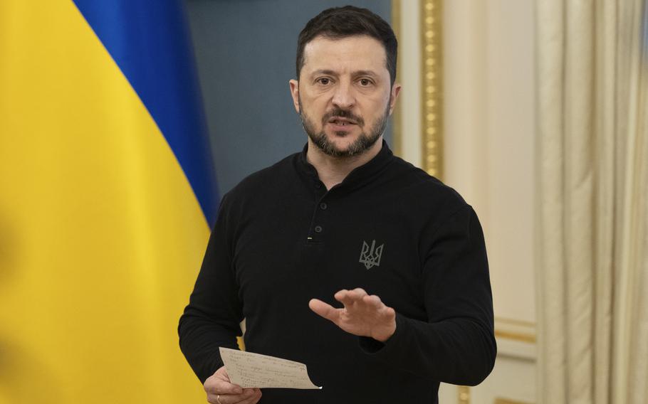 Zelenskyy holds a paper in his left hand while giving a speech.