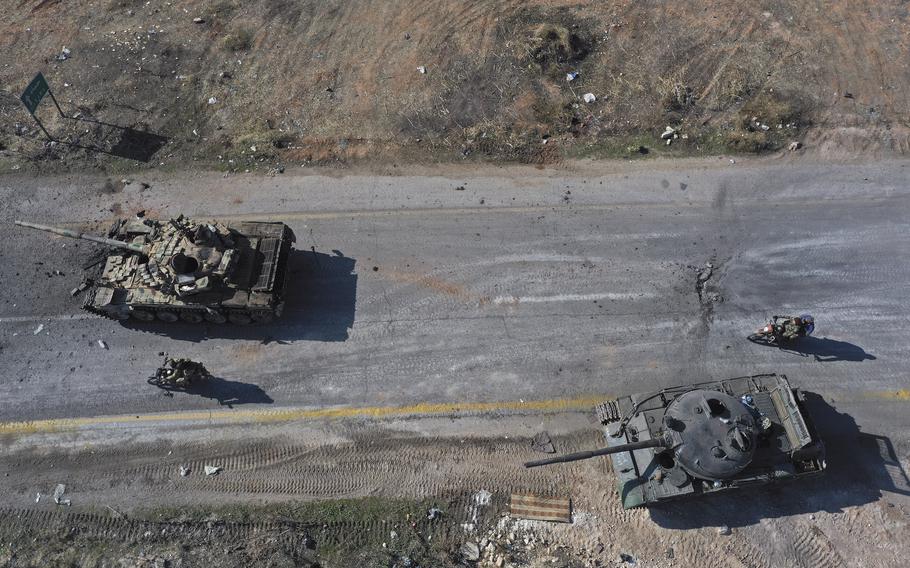 A view from above shows two abandoned Syrian army vehicles and insurgents on motorcycles driving past.