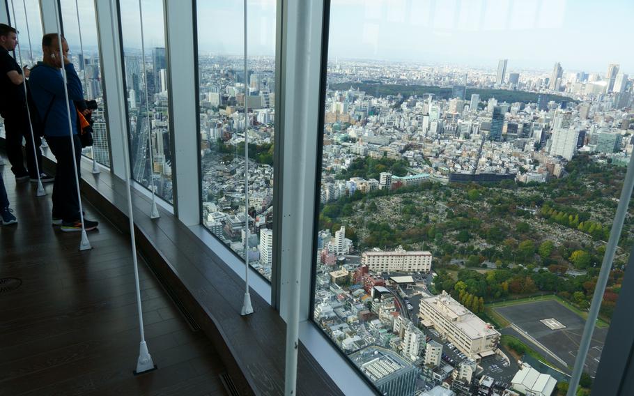 A man stands in front of floor-length windows overlooking downtown Tokyo.