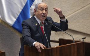 Benjamin Netanyahu stands at a podium in front of an Israeli flag and speaks into a microphone.