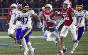 A football player carrying a football runs down the field while football players in red uniforms try to stop him.