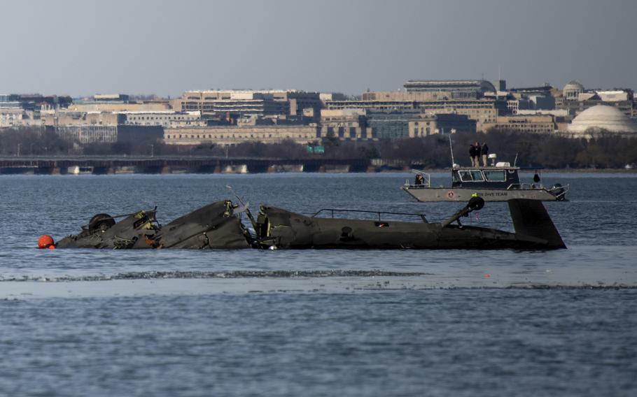 The wreckage of what appears to be a Black Hawl helicopter floats in the Potomac River, with the buildings of Washington, D.C. in the background.