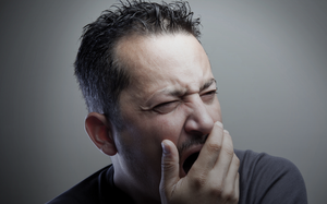 A man covers his mouth as he yawns.