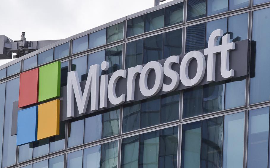 The Microsoft logo hangs on the glass windows of an office building.