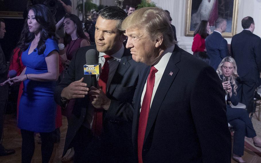 Pete Hegseth holds a microphone and speaks with Donald Trump at an event inside the White House.