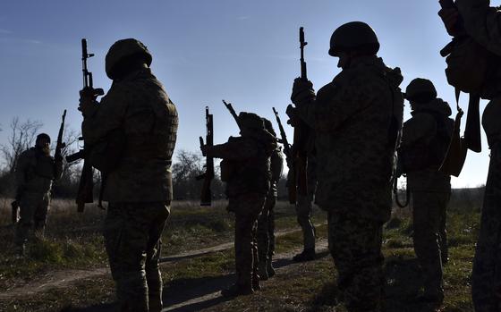 Ukrainian soldiers in combat gear and holding machine guns stand in formation during training.