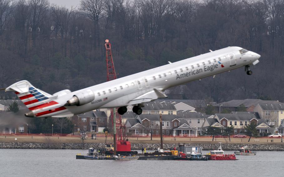 An American Airlines jet takes off with salvage crews in the background.