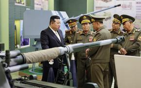 Kim Jong Un is shown at left talking to his military leaders, at right, in front of various weapons.