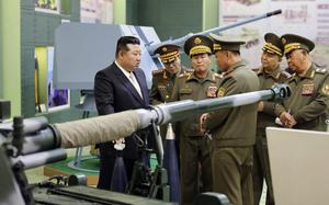 Kim Jong Un is shown at left talking to his military leaders, at right, in front of various weapons.