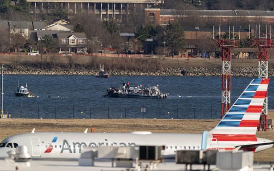 Police and coast guard boats are seen around a wreckage site in the Potomac River as an American Airlines plane passes in the foreground.