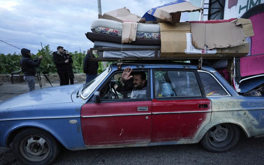 A man waves as he carries his belongings on his car as he returns home.