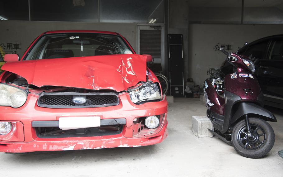 A red car with damage to the front is parked next to a purple motorcycle.