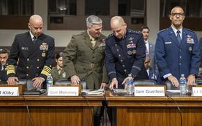 Four military officers in dress uniforms stand next to each other at a table in a congressional hearing room.