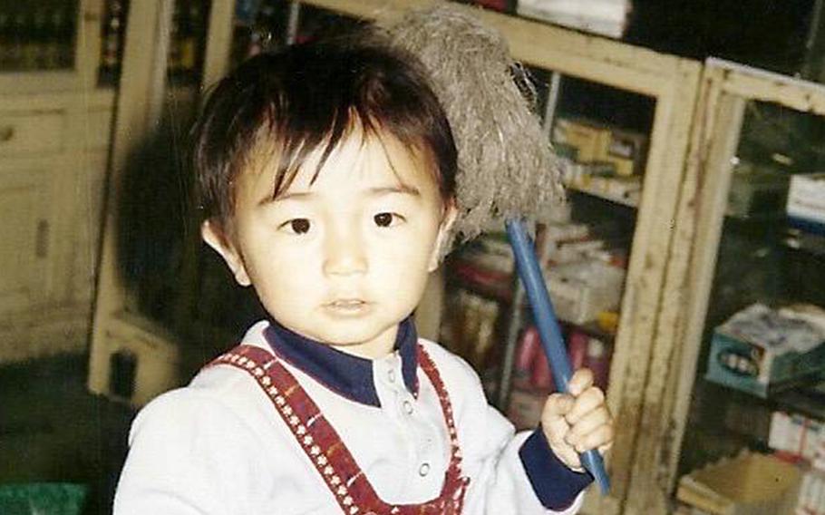 A young boy faces the camera holding a toy in his left hand. 