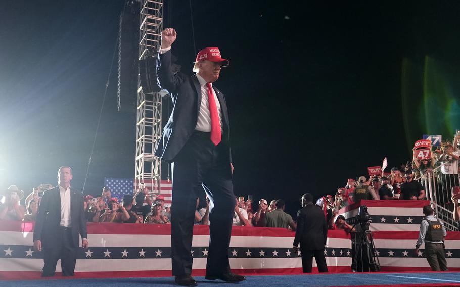 Donald Trump, wearing a red hat, raises a fist towards a crowd of people.