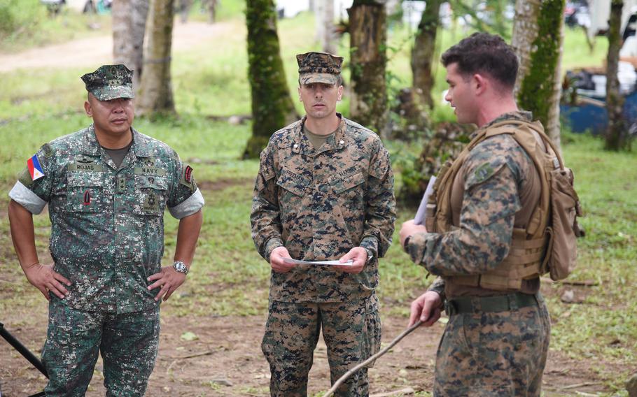 Men in uniform stand while talking in front of palm trees.