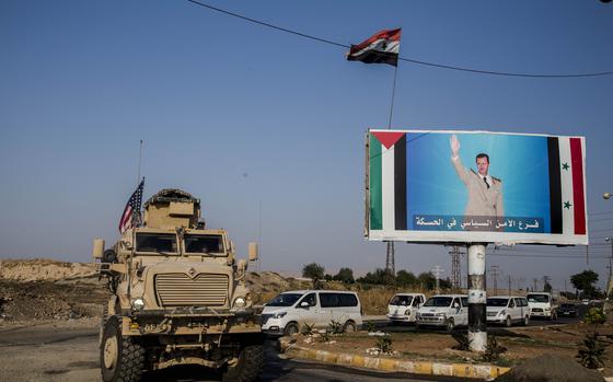 FILE - A U.S. military vehicle drives south of the northeastern city of Qamishli, on Oct. 26. 2019 likely heading to the oil-rich Deir el-Zour area where there are oil fields, or possibly to another base nearby, as it passes by a poster showing Syrian President Bashar Assad. Syria’s civil war has entered its 14th year on Friday March 15, 2024, a somber anniversary in a long-frozen conflict. The country is effectively carved up into areas controlled by the Damascus government, various opposition groups and Kurdish forces. (AP Photo/Baderkhan Ahmad, File)