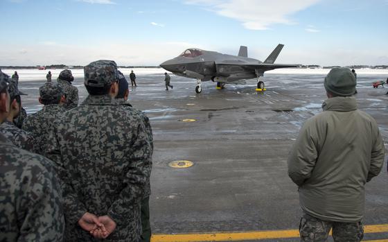 Japanese military members watch a fighter jet land on an airfield.