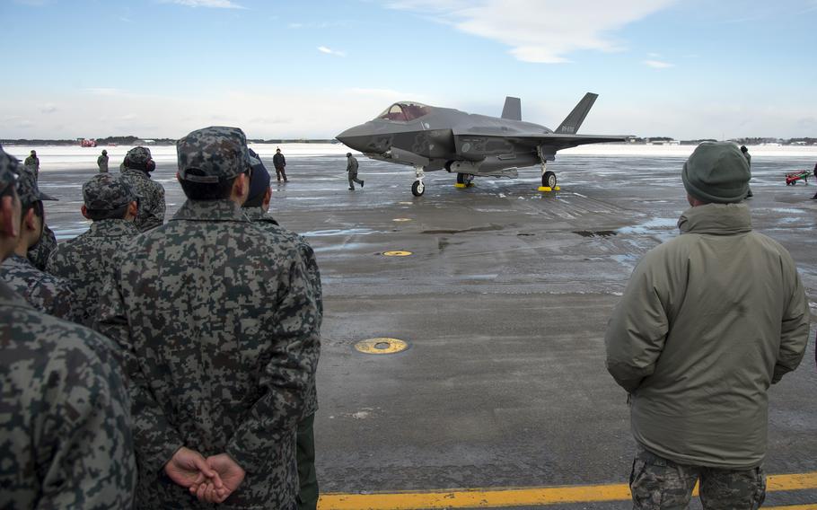 Japanese military members watch a fighter jet land on an airfield.