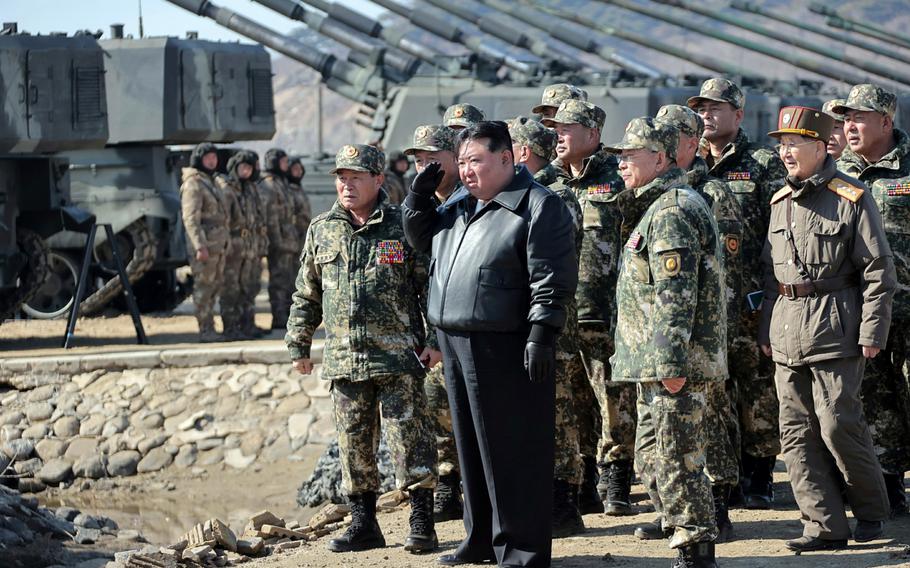 The North Korean leader stands with a group of military members outside, observing a training.