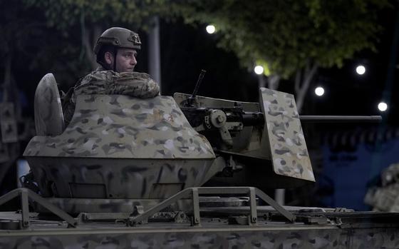 A soldier wearing a helmet sits in a gun turret atop an armored vehicle.