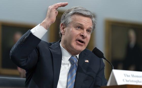 A man in a dark suit gestures with his hand while seated in front of a microphone during a congressional hearing.