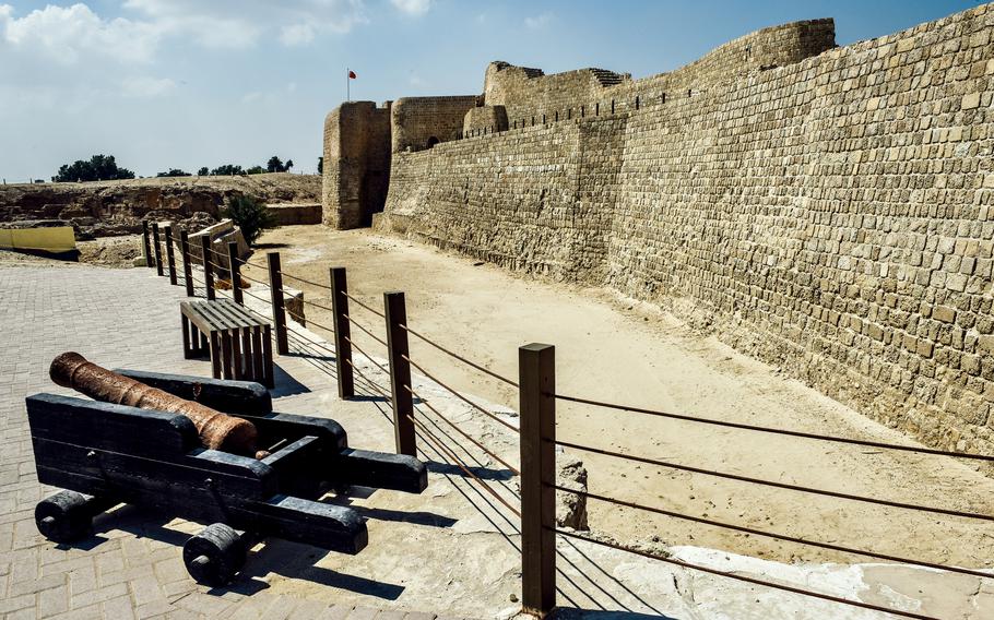 A small cannon is on display outside Bahrain Fort in front of a large brick defense wall. Cannons were used by the Portuguese, who occupied Bahrain in 1521, using the fort as part of their strategic defense.