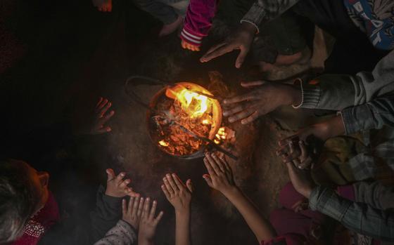 Small hands reach towards a small burning fire in the center of a pit.