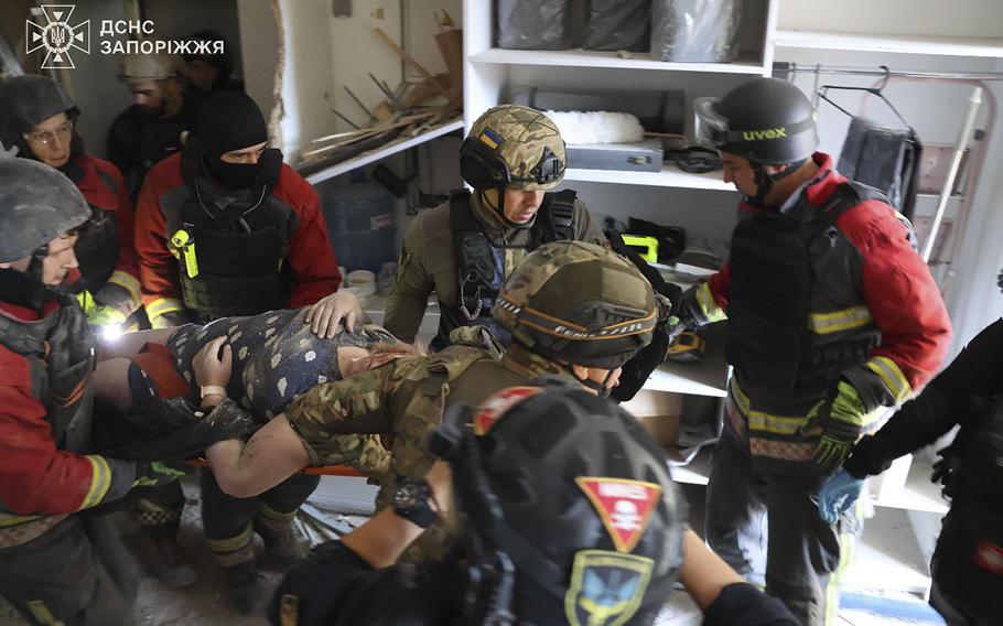 Rescuers wearing helmets evacuate a resident from an apartment in Zaporizhzhia, Ukraine.