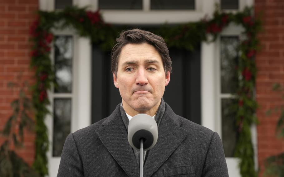 Justin Trudeau is seen in the center of the photo with a microphone in front of him, obscuring his neck.