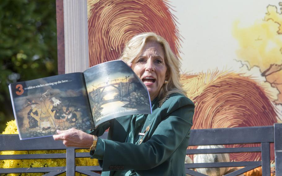 A woman sitting on an outdoor bench reads a book aloud to a crowd.