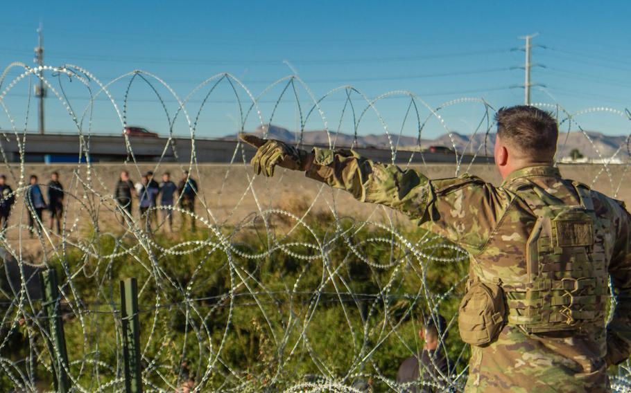 A Texas National Guard soldier stands at a barbed-wire barrier and blocks a group of migrants from crossing into the U.S. between legal ports of entry near El Paso, Texas. 