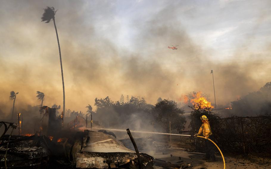 A firefighter sprays a hose at a burning structure.