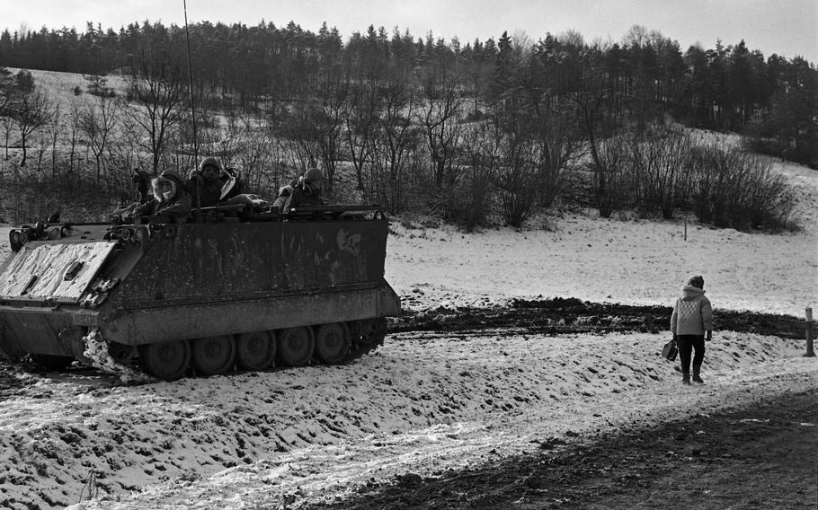 A woman walking through the snow past an M113 