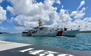 A Coast Guard cutter sails on teal water with white clouds and a blue sky in the background. 