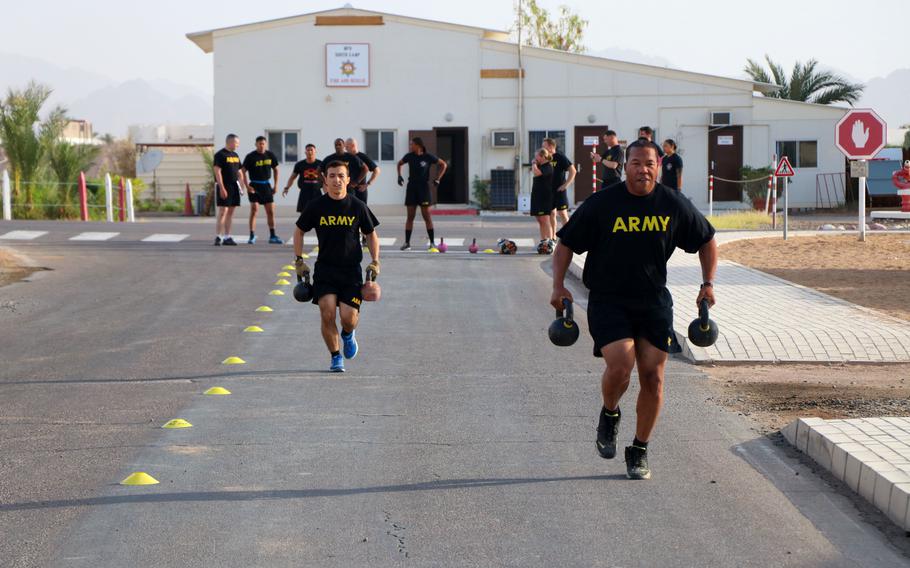 U.S. soldiers wearing black-and-gold physical training uniforms run with kettlebells.